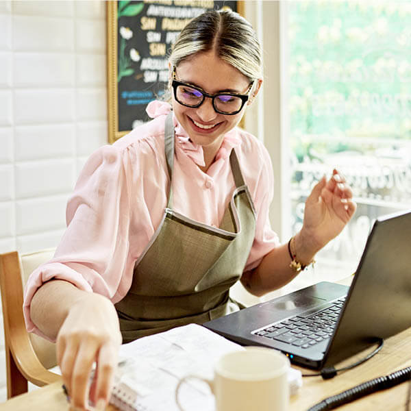 Mujer propietaria de un negocio con gafas usando una laptop y sonriendo