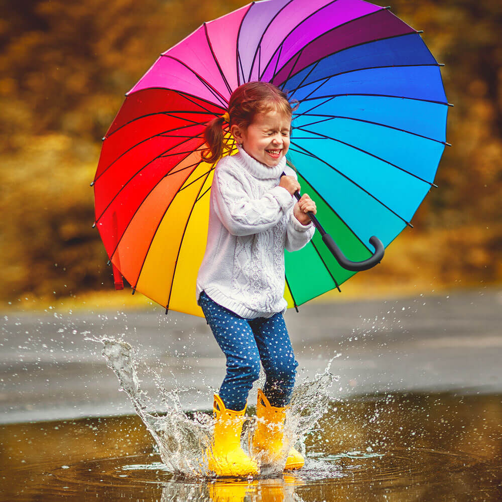 Girl with rainbow umbrella jumping in a puddle